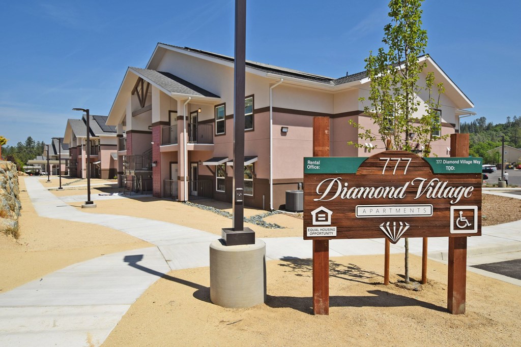 A sign for Diamond Village Apartment is in front of some buildings.