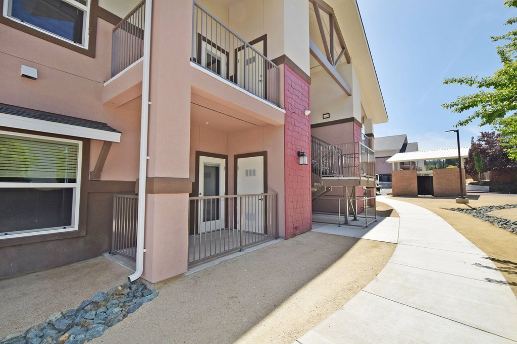 A building with a pink and beige facade has a balcony and a door.