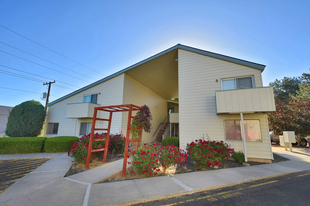 A house with a red pergola and flower bed in front.