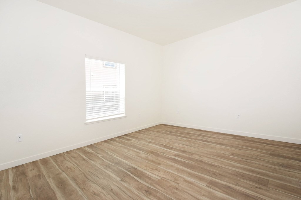 A room with wooden flooring and a window with blinds.