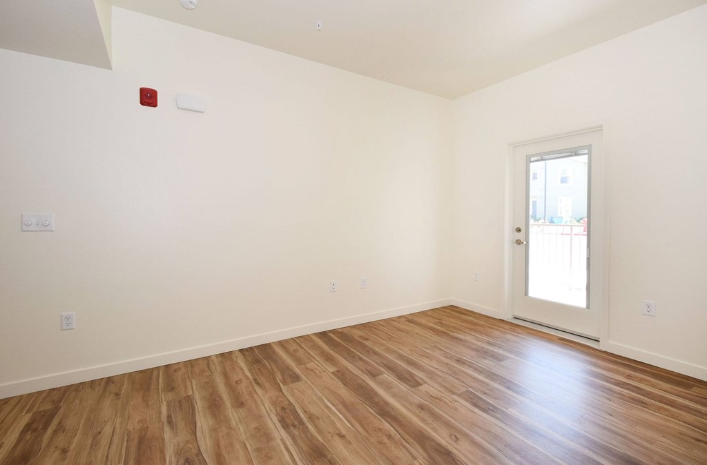A room with a wooden floor and a door leading to a balcony.