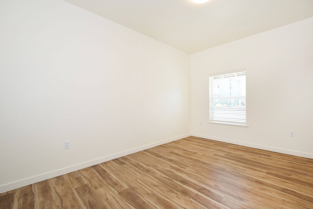 A room with wooden flooring and a window with blinds.
