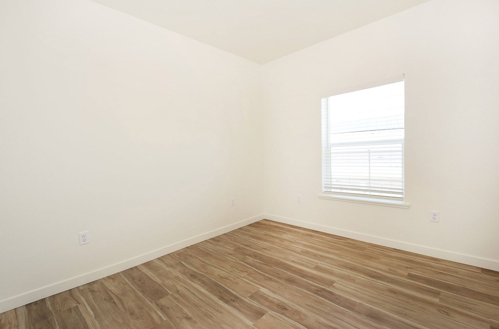 A room with wooden flooring and a window with blinds.