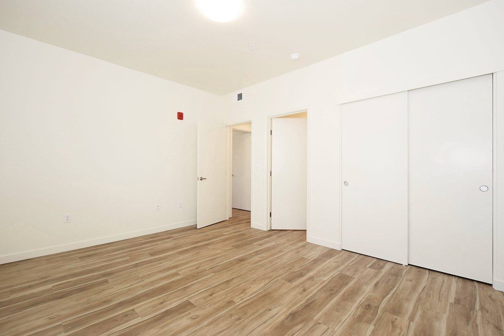 A room with white walls and wooden flooring with a doorway leading to another room.