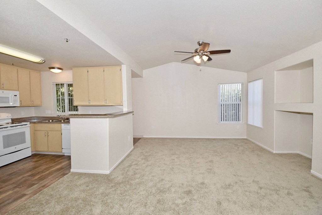 an empty living room and kitchen with a ceiling fan