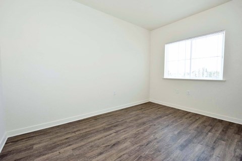 a bedroom with white walls and wood floors and a window