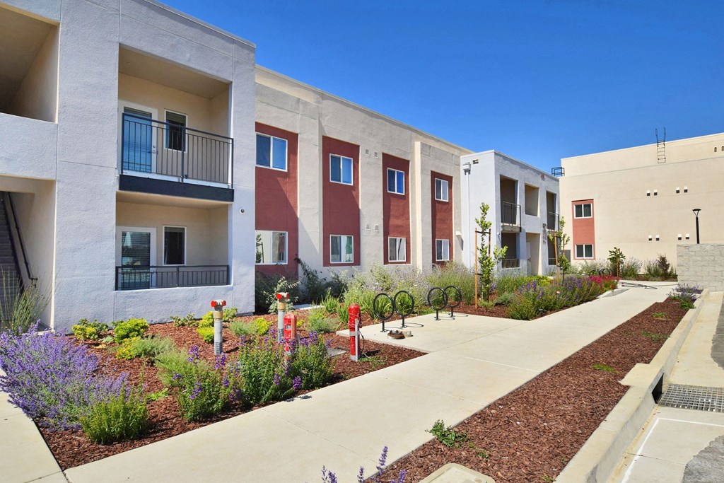 a row of apartment buildings with a sidewalk and landscaping