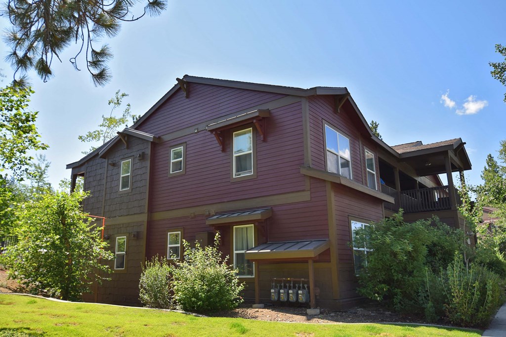 the front of a red house with a lawn and trees