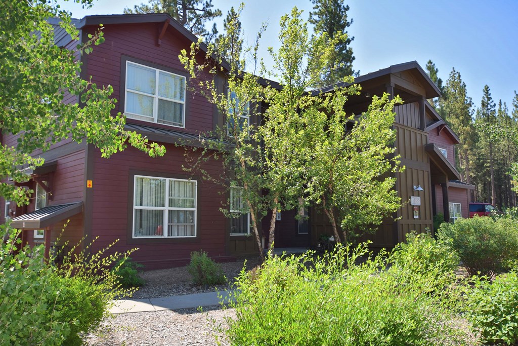 the front of a red house with trees and bushes