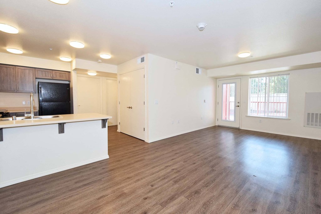 an empty living room with a kitchen in the background