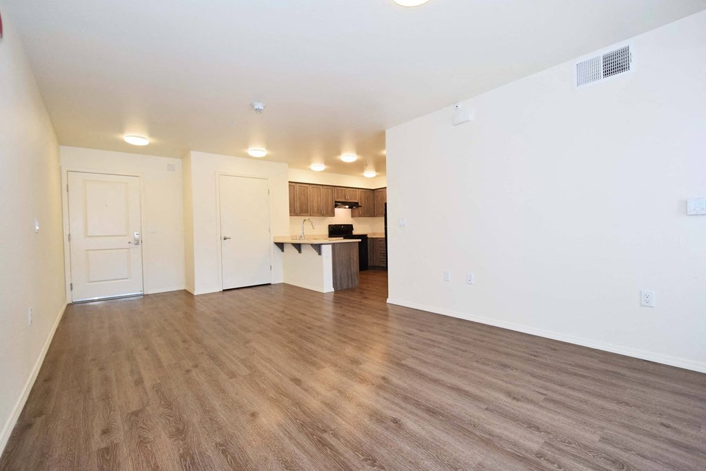 an empty living room with a kitchen in the background
