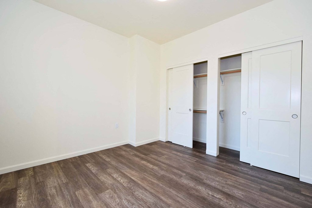 a bedroom with white walls and wood floors and closets
