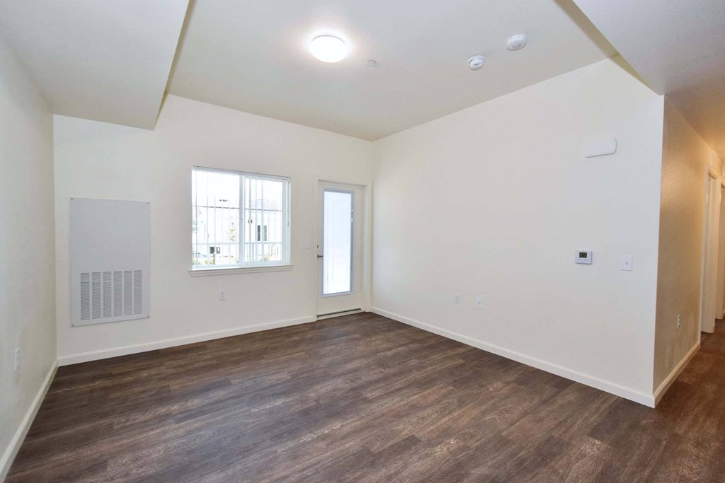 a living room with white walls and wood flooring and a window
