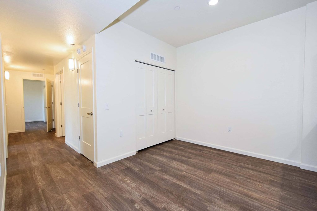a bedroom with white walls and wood flooring and a door to a hallway