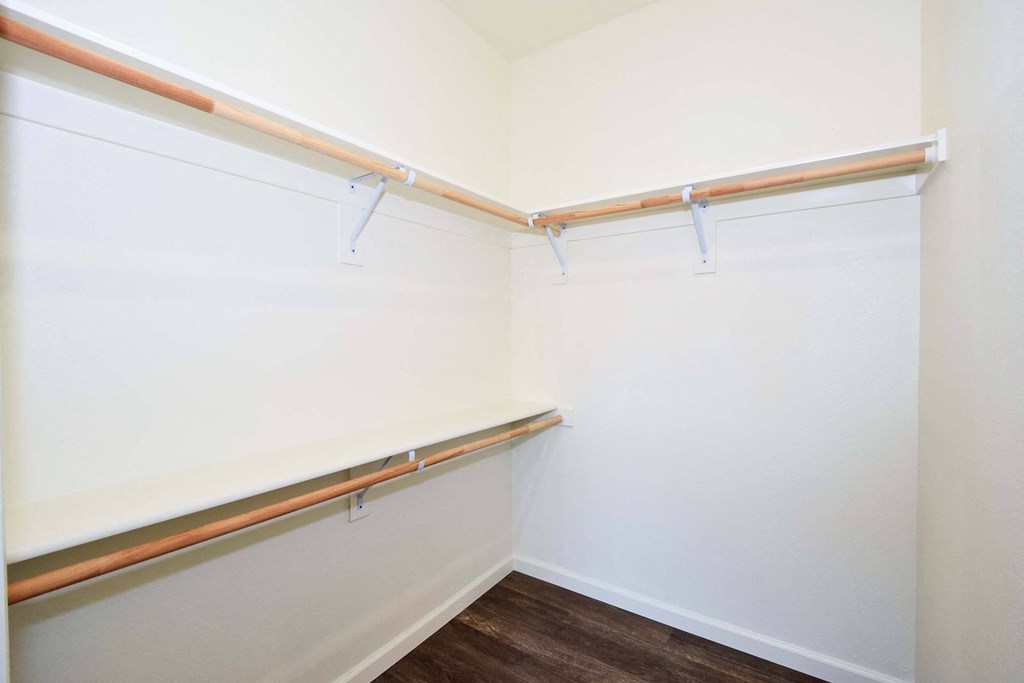 a walk in closet with white walls and a wood floor