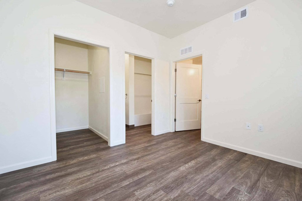 a bedroom with white walls and wood floors and closets