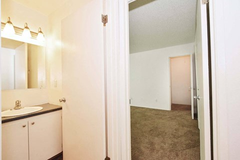 a bathroom with a sink and a mirror and a hallway to a bedroom