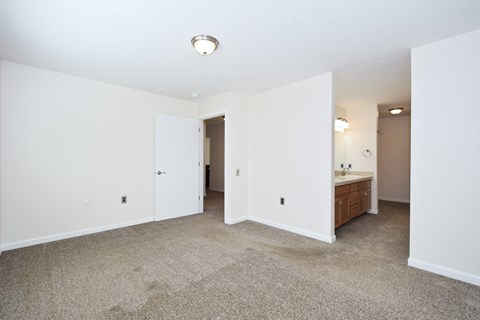a bedroom with white walls and carpet and a bathroom with a sink and a mirror