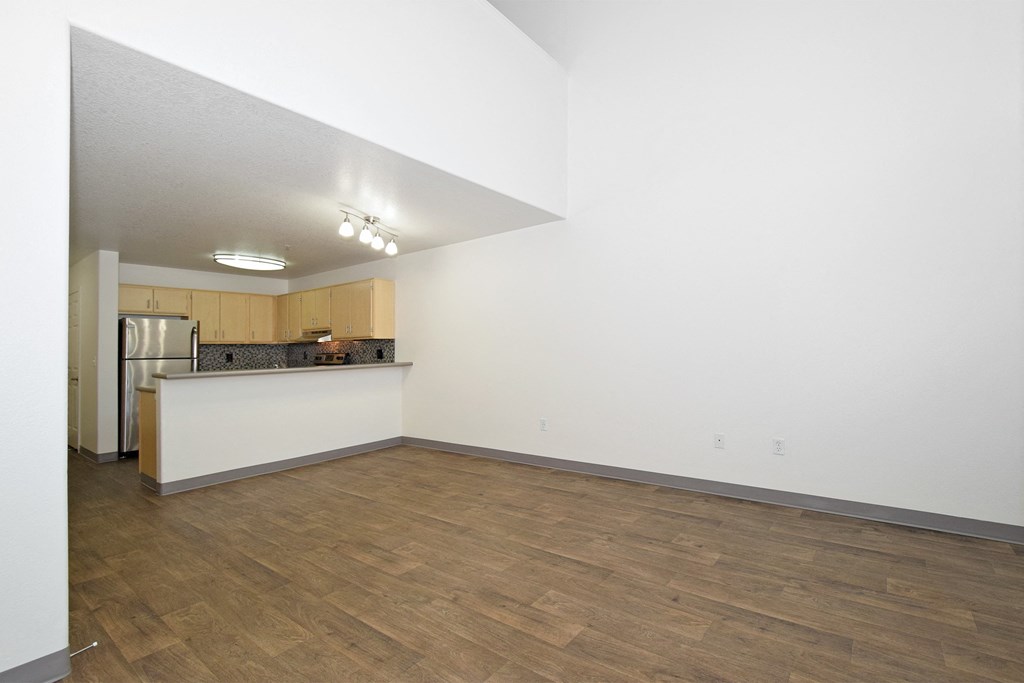an empty living room and kitchen with wood floors and white walls