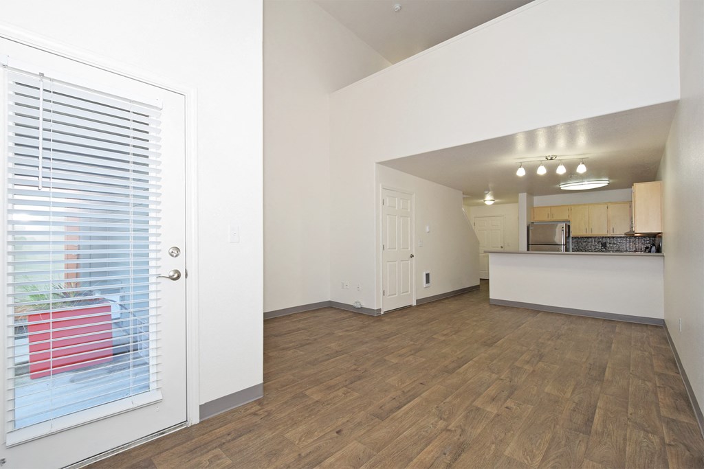 the living room and kitchen of an apartment with white walls and wood flooring
