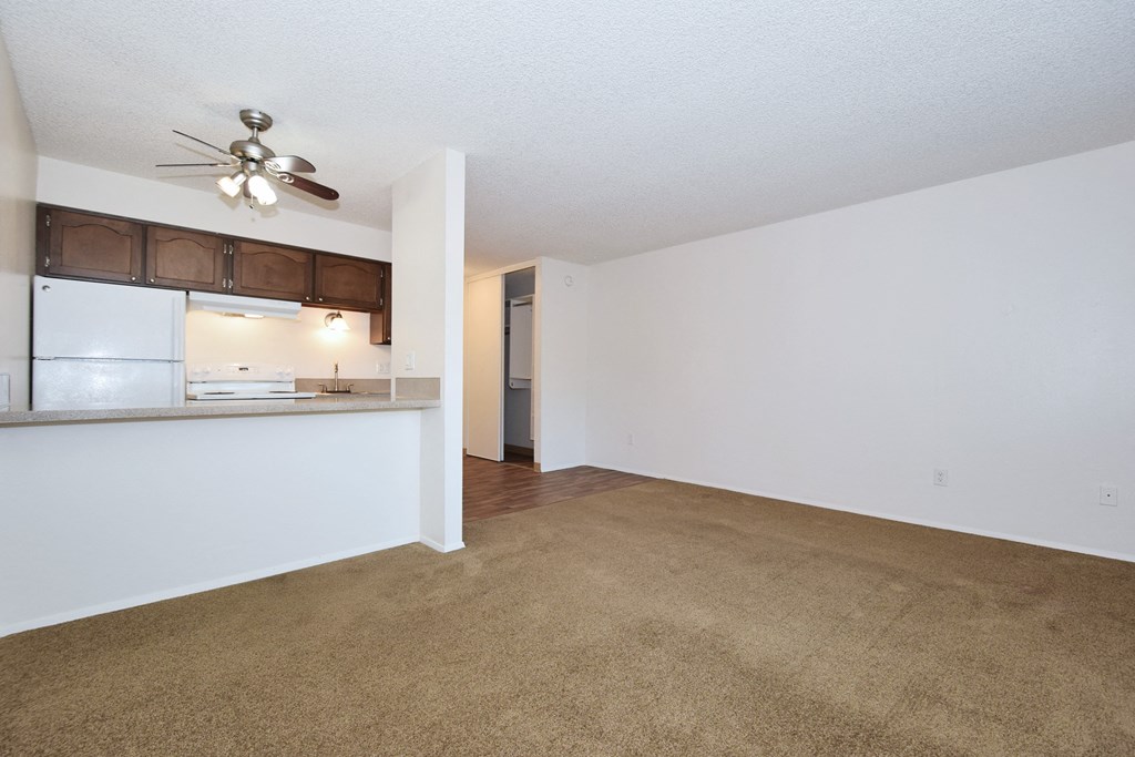 an empty living room with a kitchen and a ceiling fan