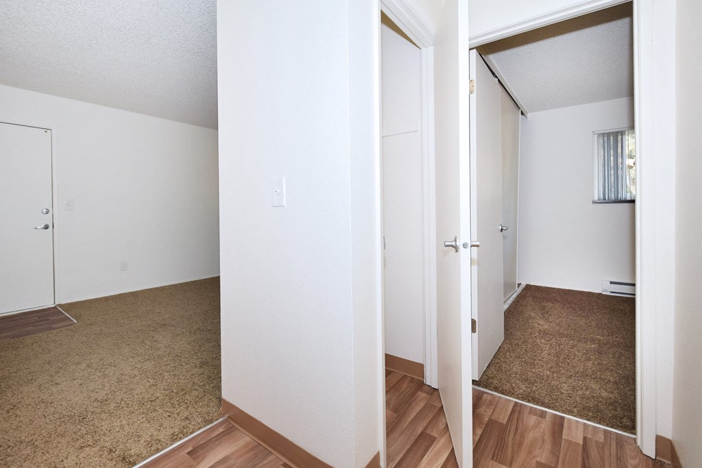 the living room and bedroom of an apartment with wood flooring and white walls