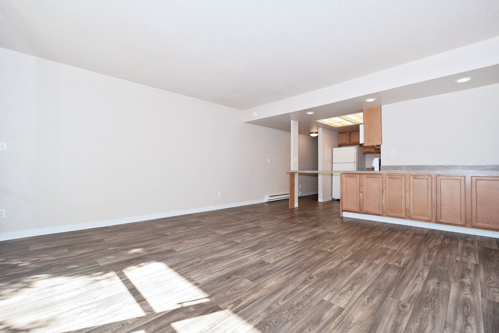 the living room and kitchen of an empty apartment with wood flooring
