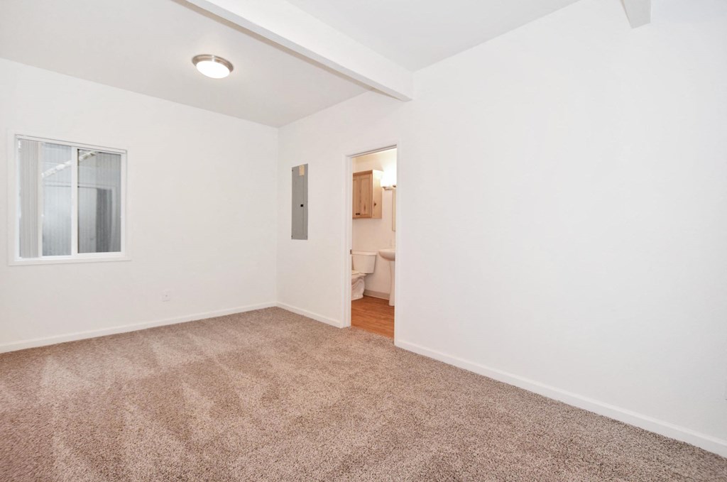 a bedroom with white walls and carpet and a door to a bathroom