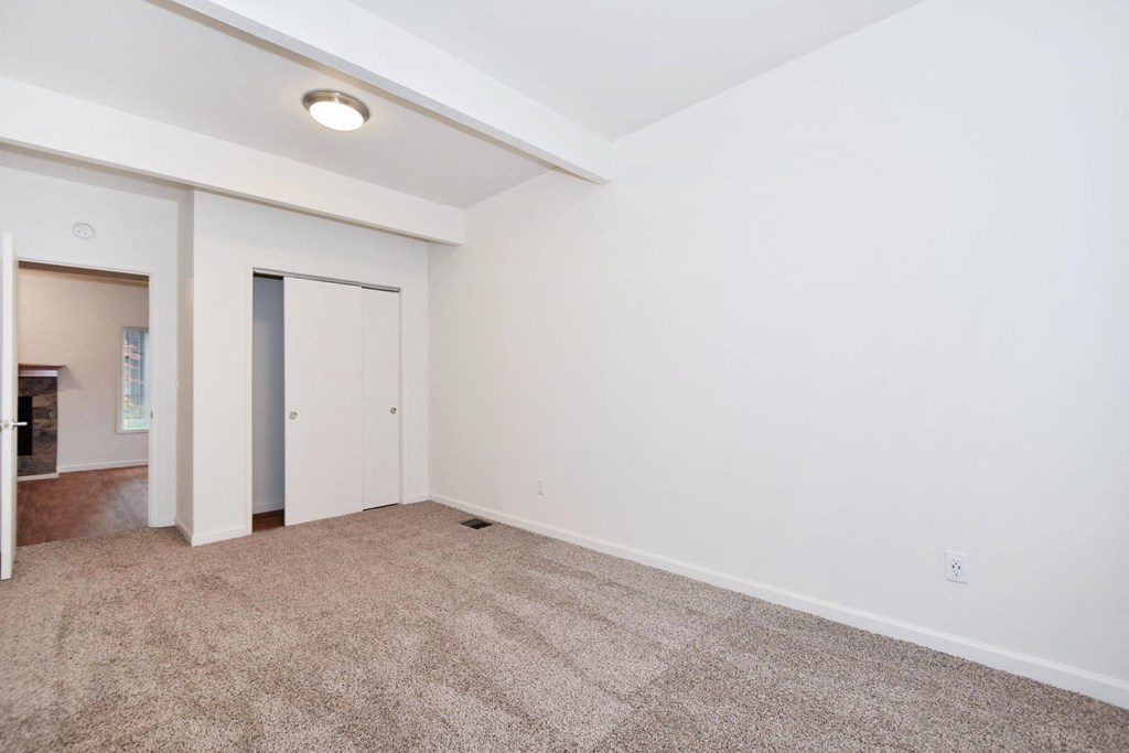 a living room with white walls and carpet and a door to a closet