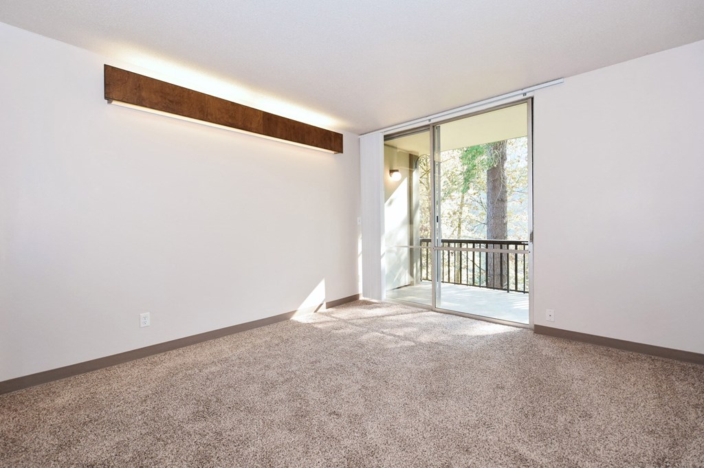 a living room with carpet and a sliding glass door to a balcony