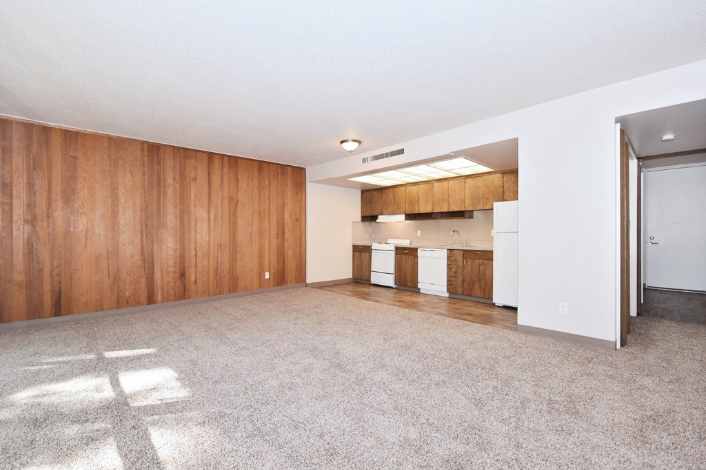the living room and kitchen of an apartment with white appliances and wood walls