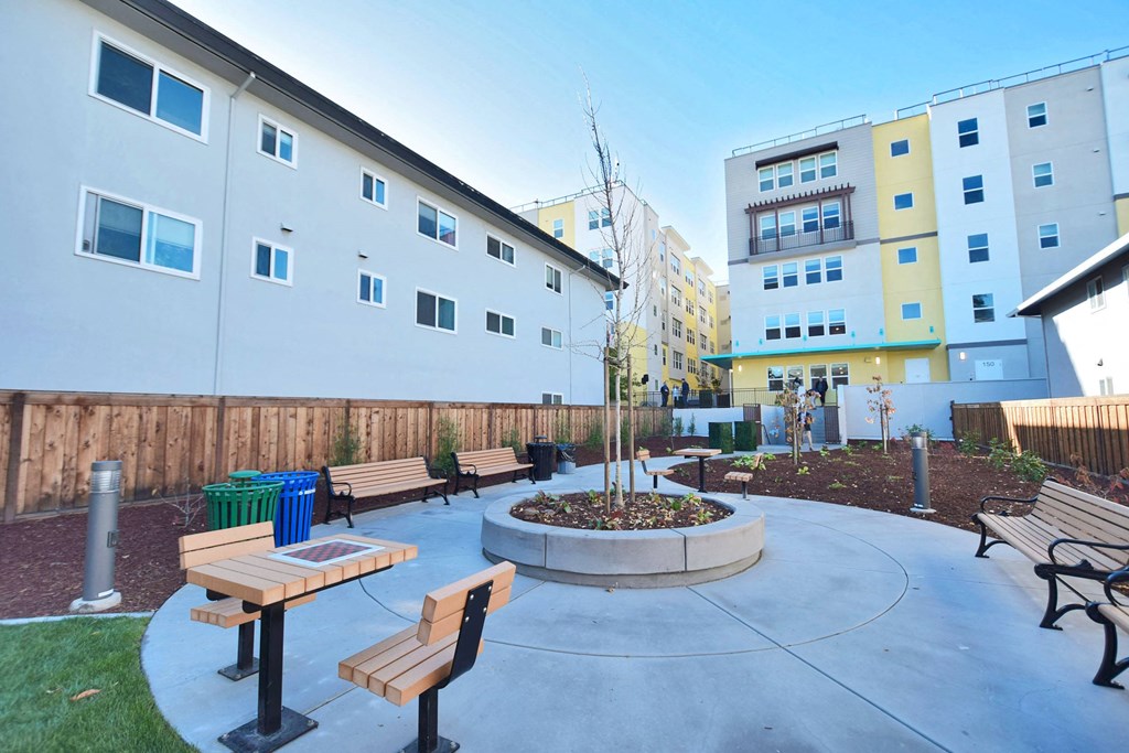 a courtyard with benches and a fire pit in front of some buildings
