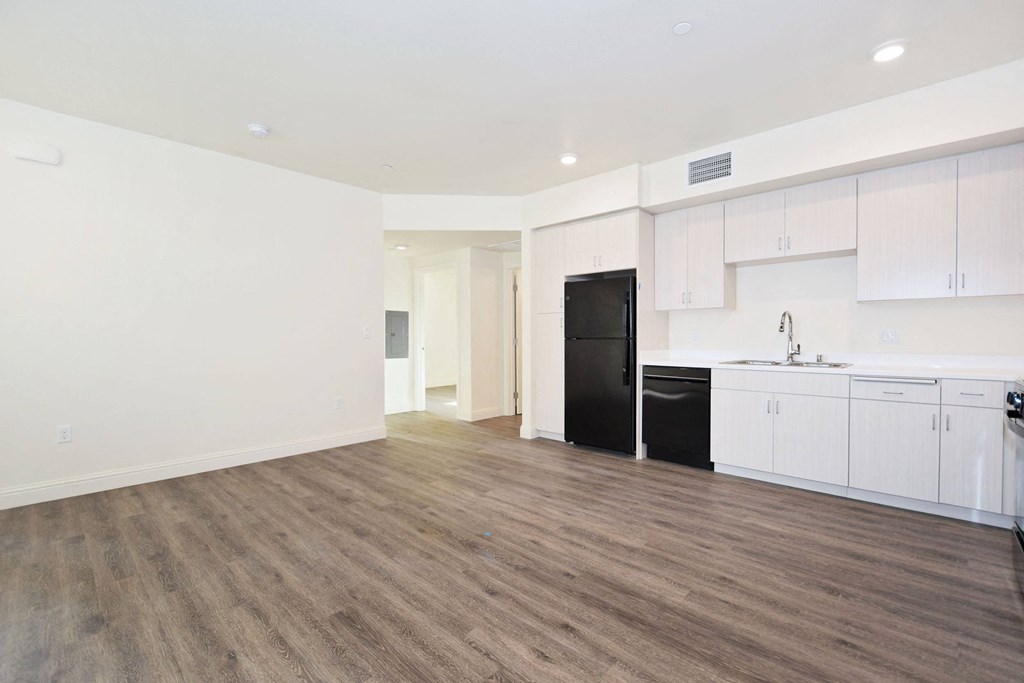 the living room and kitchen of an apartment with white cabinets and a black refrigerator