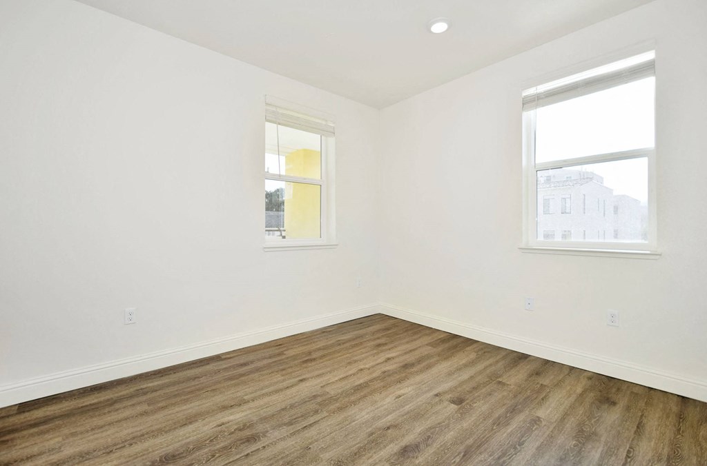 an empty room with wood floors and two windows