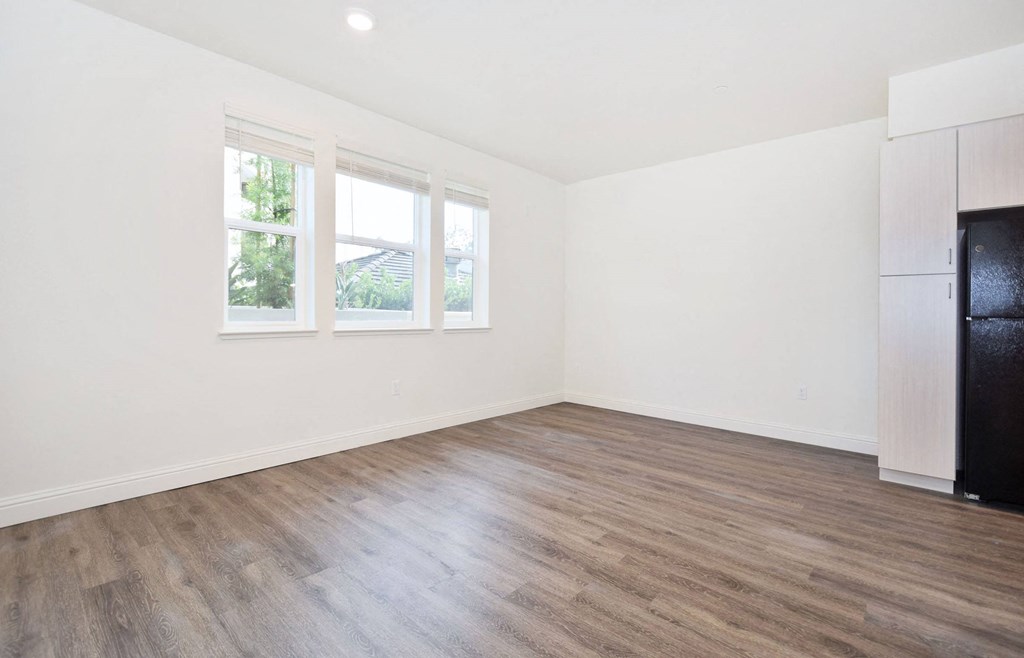 an empty living room with a refrigerator and a window