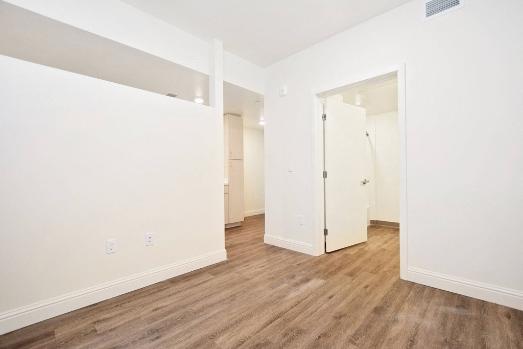 a bedroom with white walls and wood flooring and a closet