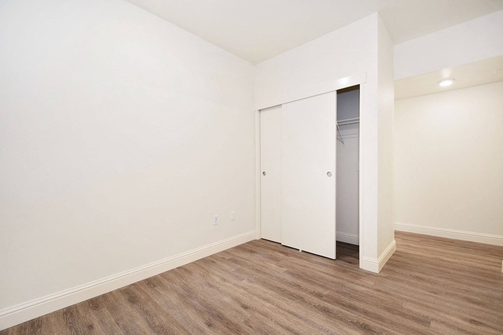 a bedroom with white walls and wood flooring and a closet