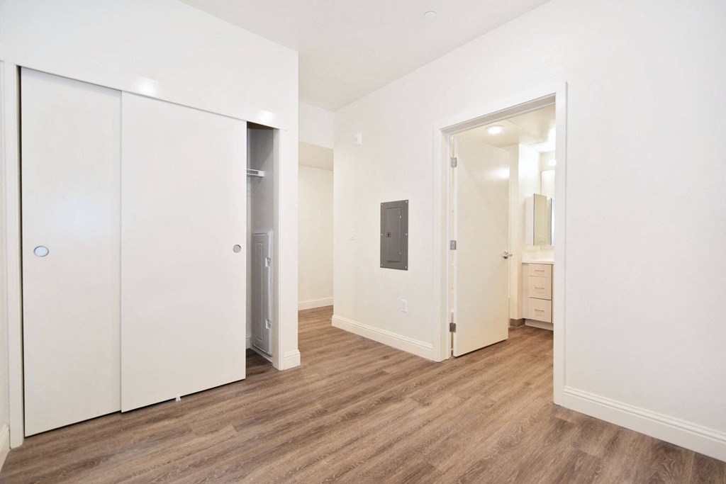 a bedroom with white walls and wood flooring and a closet