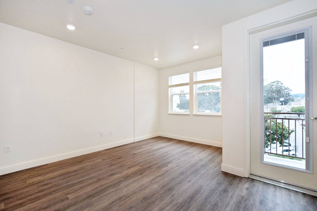 a living room with white walls and wood floors and a balcony