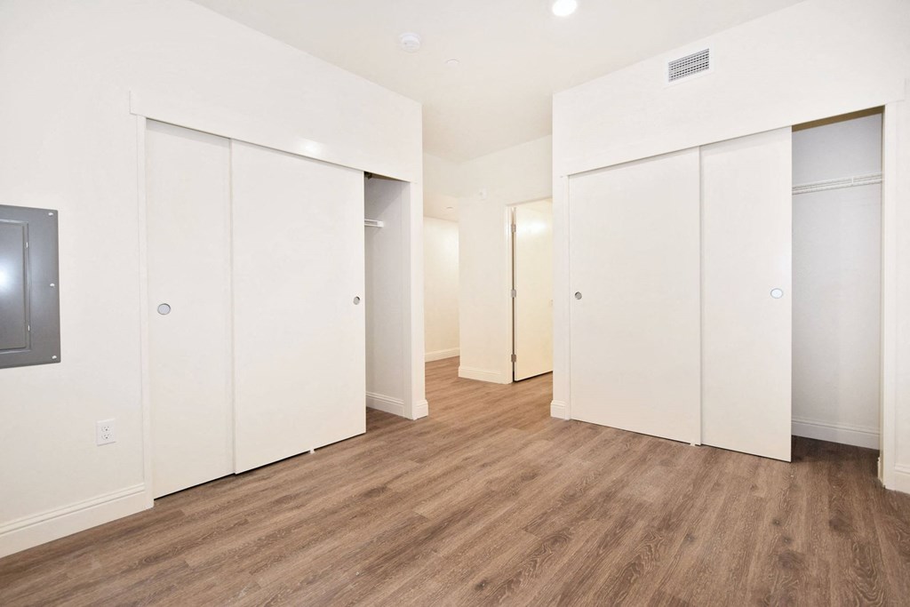 a bedroom with white walls and wood flooring and closet space
