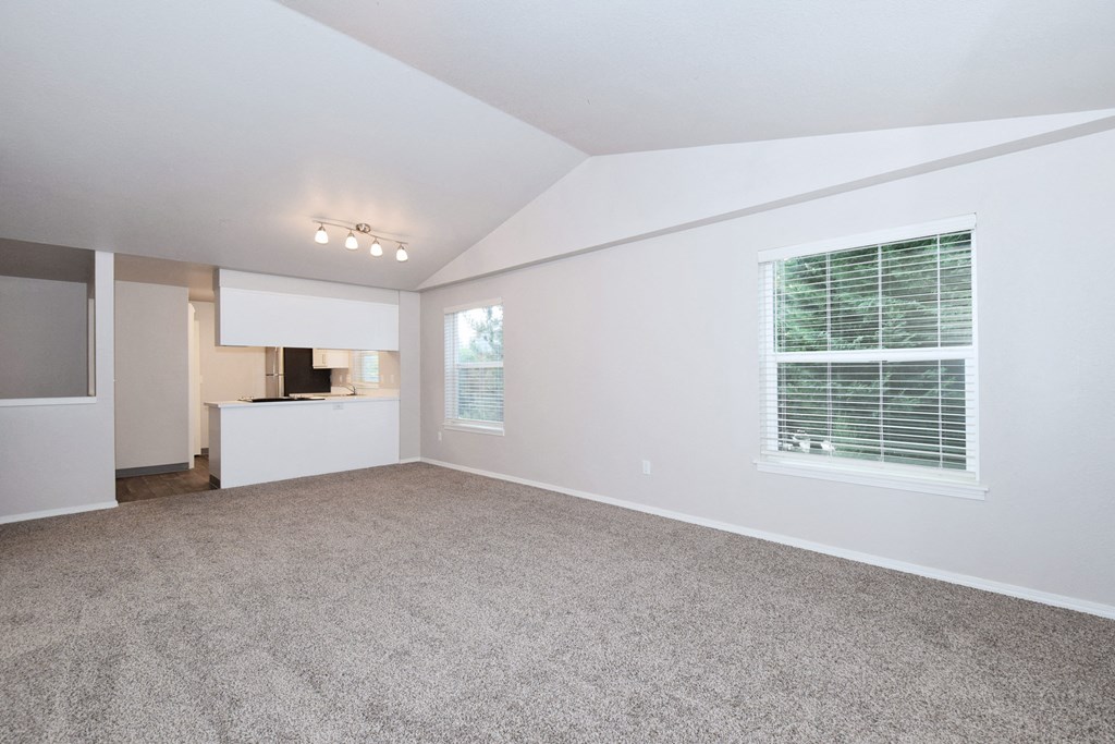 an empty living room with a window and a kitchen