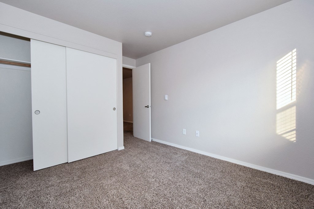 a bedroom with white walls and carpet and white closet doors