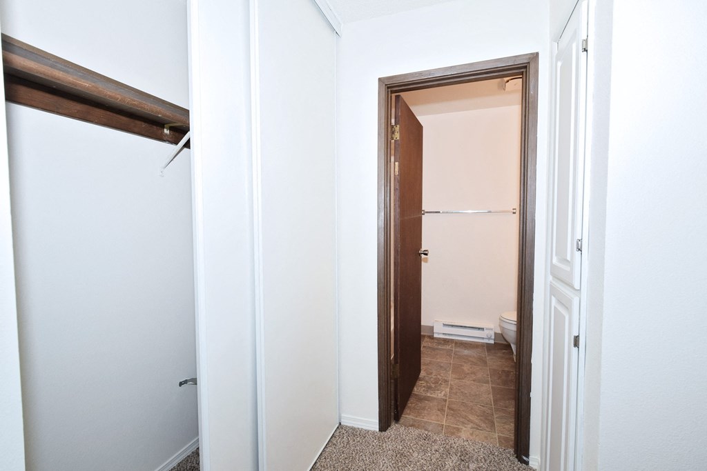 a walk in closet in a bedroom with white walls and a tiled floor