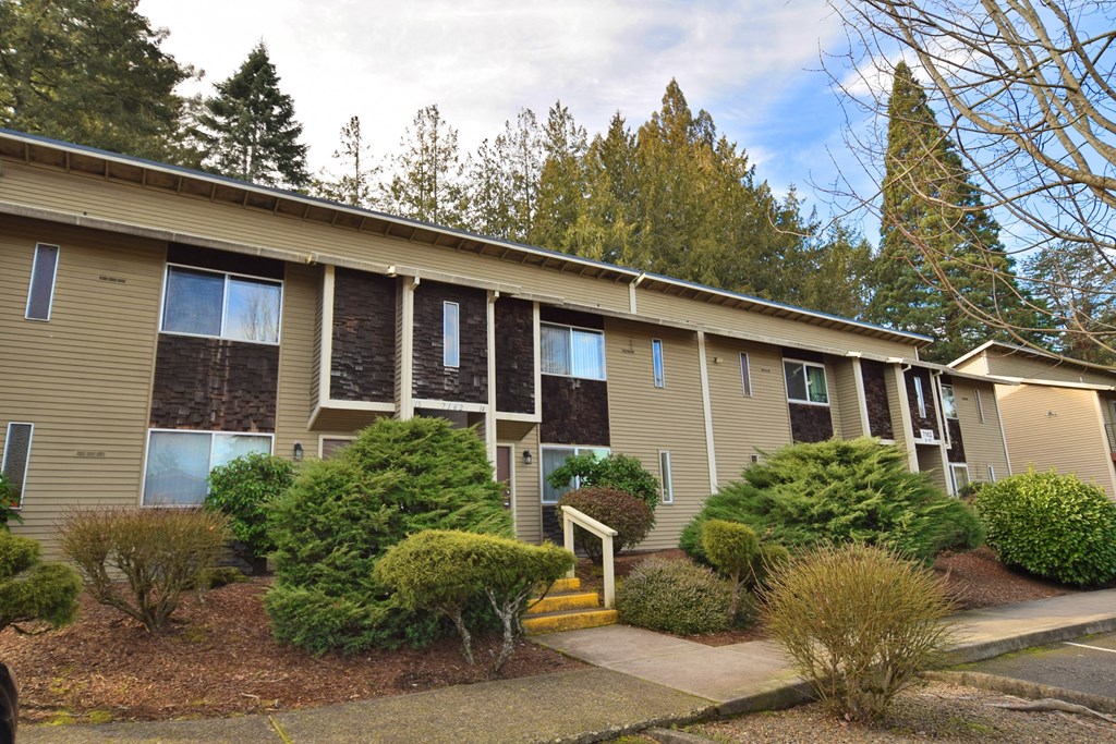 an exterior view of a tan apartment building with trees in the background