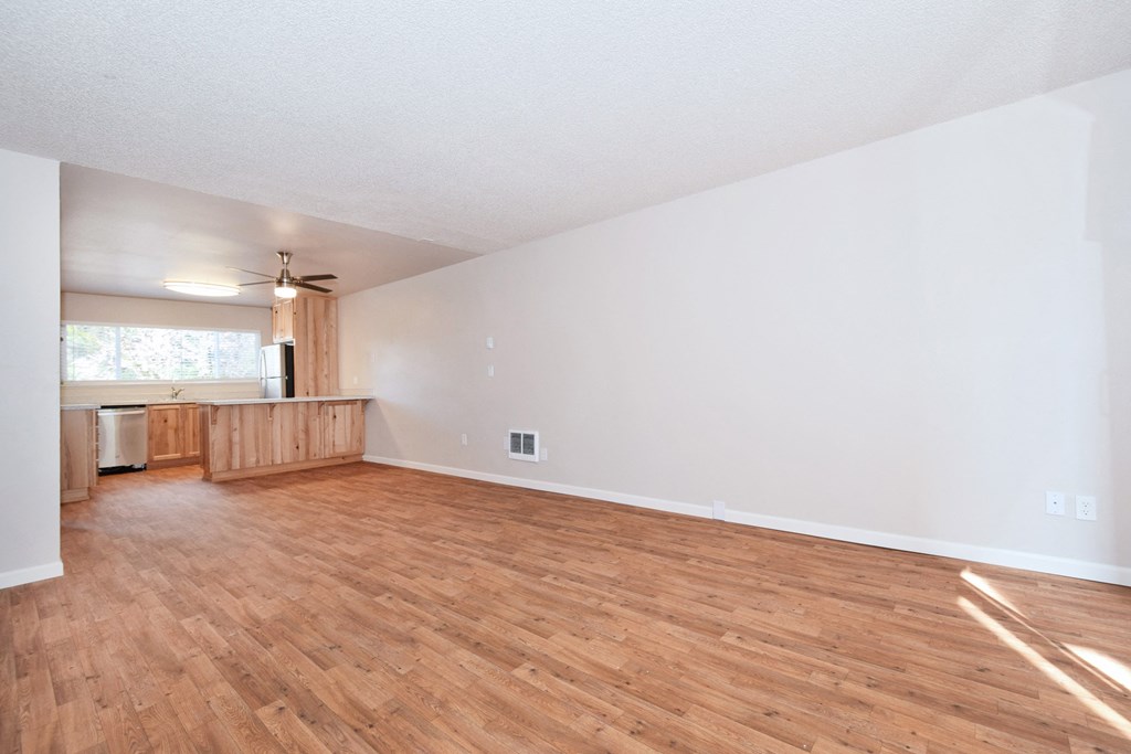 an empty living room with a kitchen in the background