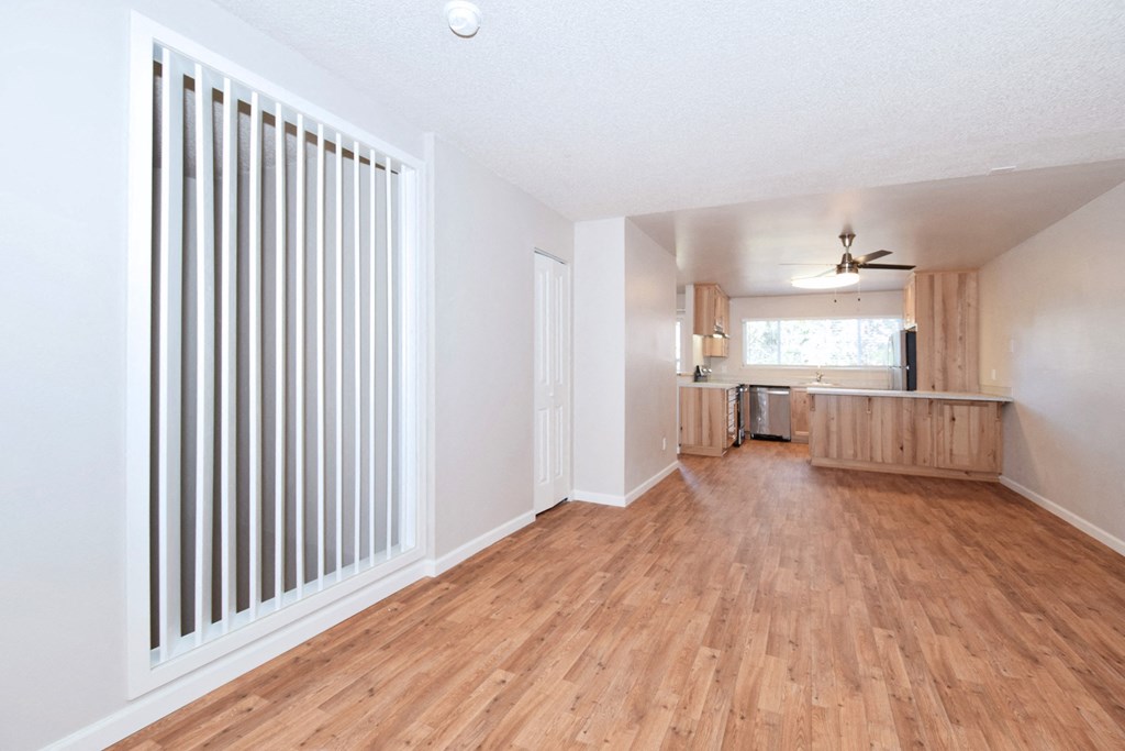 an empty living room with a kitchen in the background