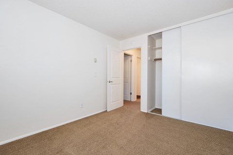 a bedroom with white walls and carpet and a door to a closet