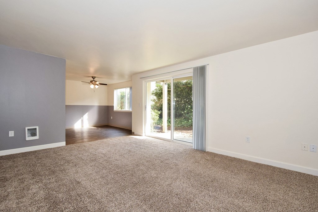 an empty living room with a sliding glass door and a ceiling fan