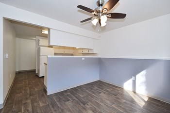 an empty living room with a ceiling fan and a kitchen in the background - Photo Gallery 60