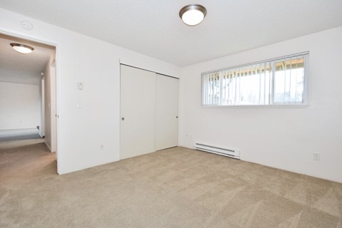 the living room and bedroom of an apartment with carpeting and a window